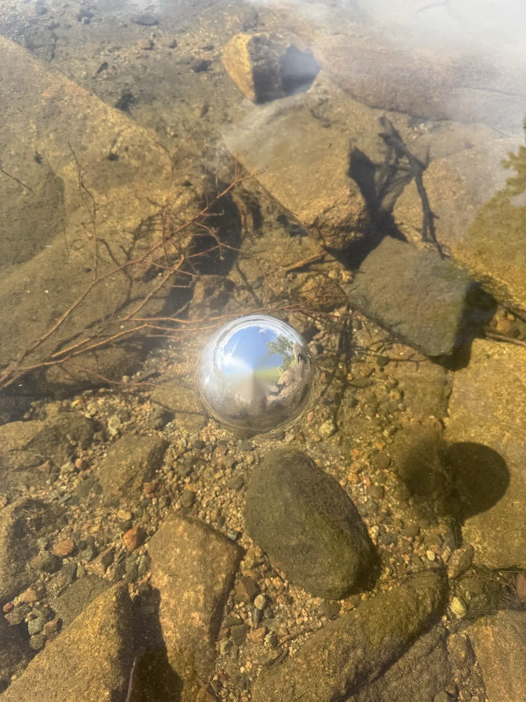 Mirror-polished stainless steel float ball reflecting the sky in a clear stream